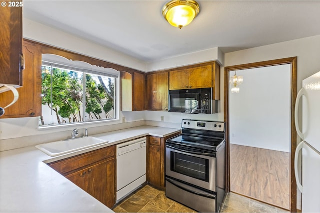 kitchen with brown cabinetry, an inviting chandelier, white appliances, light countertops, and a sink