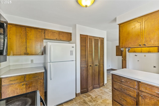 kitchen with brown cabinetry, freestanding refrigerator, electric range, and light countertops
