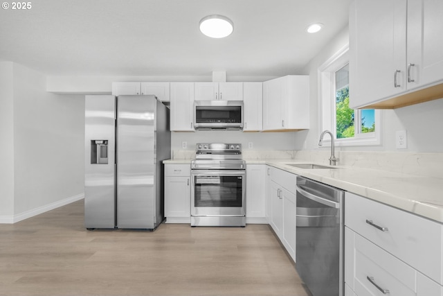 kitchen with stainless steel appliances, a sink, light countertops, light wood-style flooring, and white cabinets