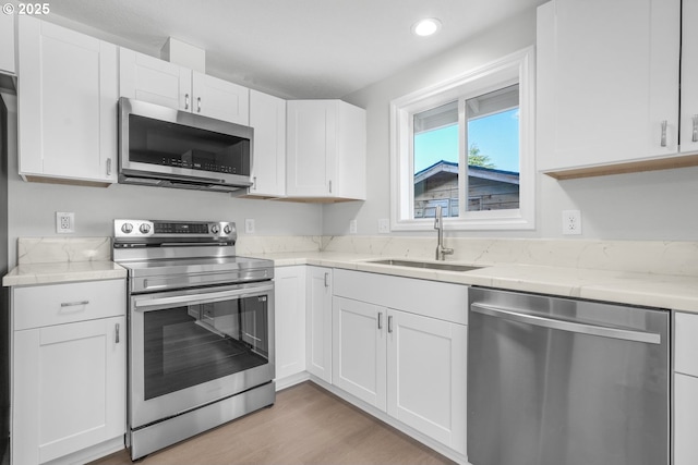 kitchen featuring appliances with stainless steel finishes, a sink, white cabinetry, recessed lighting, and light wood-style flooring