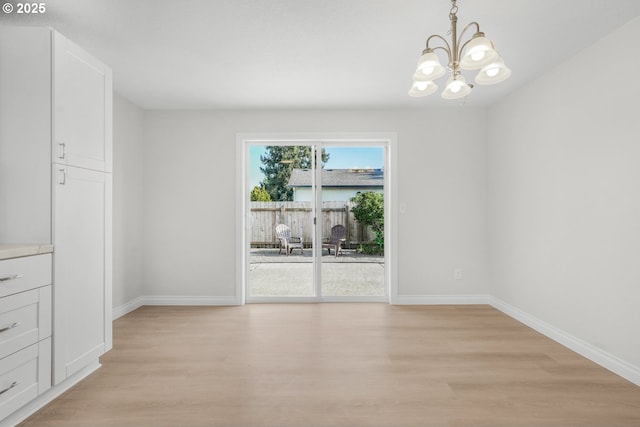 unfurnished dining area with a chandelier, light wood-style floors, and baseboards