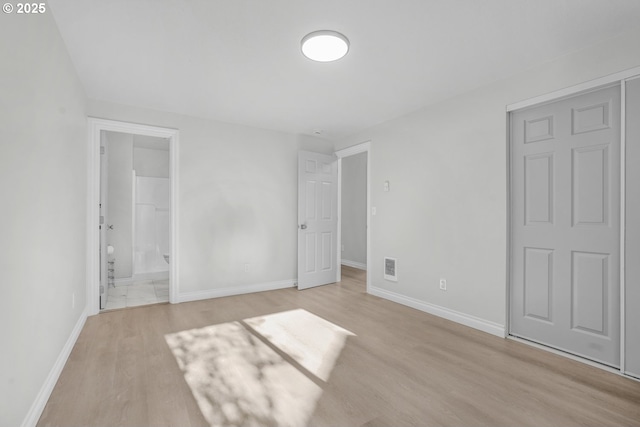 unfurnished bedroom featuring light wood-style flooring, baseboards, and ensuite bath