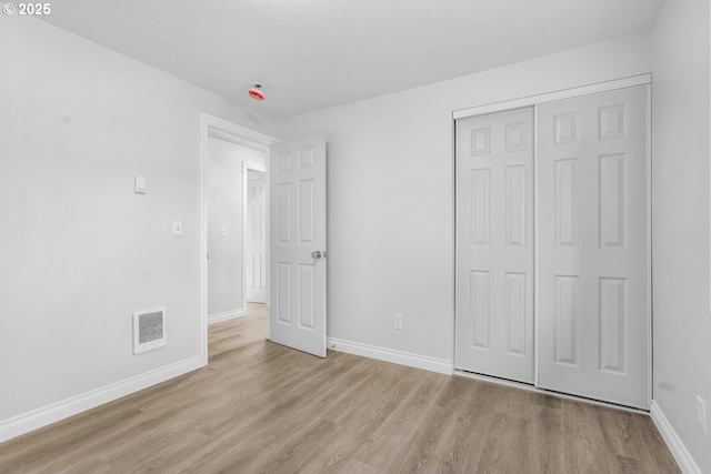 unfurnished bedroom with light wood-style flooring, baseboards, and a closet