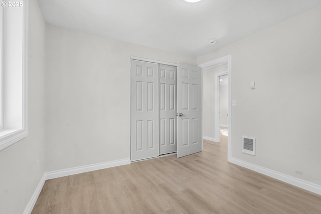 unfurnished bedroom featuring light wood finished floors, baseboards, and a closet