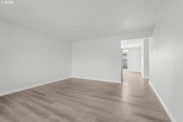 unfurnished room featuring a chandelier, light wood finished floors, and baseboards