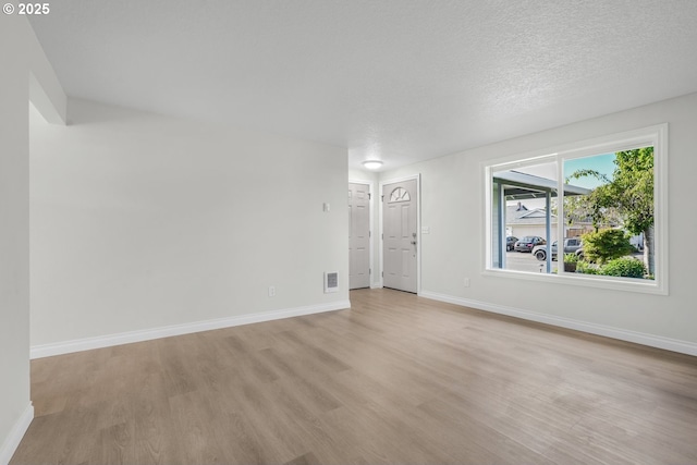 unfurnished living room featuring light wood finished floors, baseboards, and a textured ceiling
