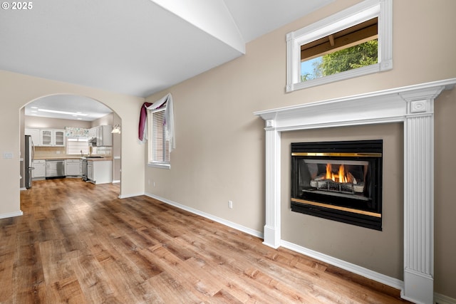 1670 NE Jackson School Rd, Hillsboro, OR 97124 - unfurnished living room with light wood-style floors, arched walkways, baseboards, and a warm lit fireplace