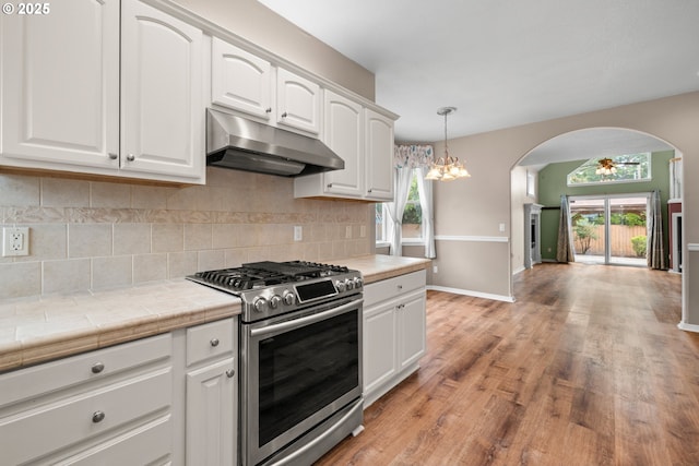 1670 NE Jackson School Rd, Hillsboro, OR 97124 - kitchen with stainless steel range with gas cooktop, under cabinet range hood, arched walkways, baseboards, and tile counters