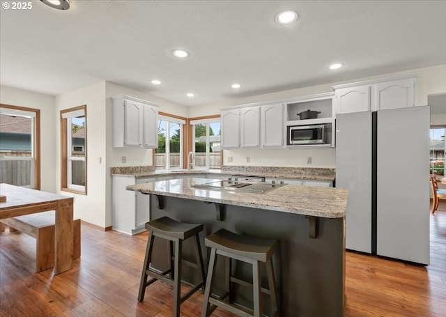 817 NW 141st St, Vancouver, WA 98685 - kitchen with stainless steel microwave, white cabinetry, freestanding refrigerator, a breakfast bar area, and wood finished floors