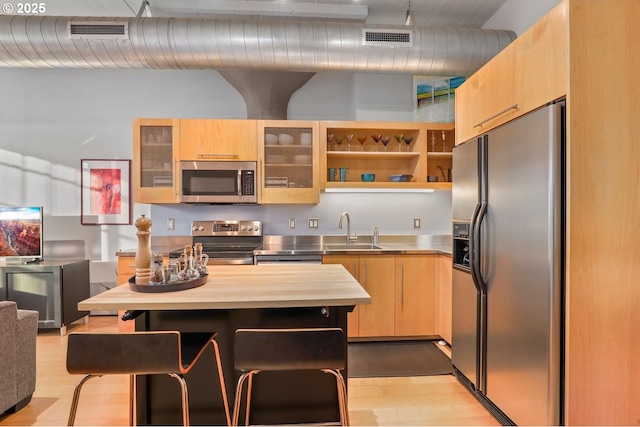 kitchen with light hardwood / wood-style floors, butcher block countertops, appliances with stainless steel finishes, light brown cabinets, and sink