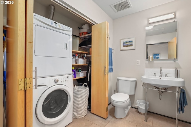 laundry area featuring sink, stacked washing maching and dryer, and light tile patterned flooring