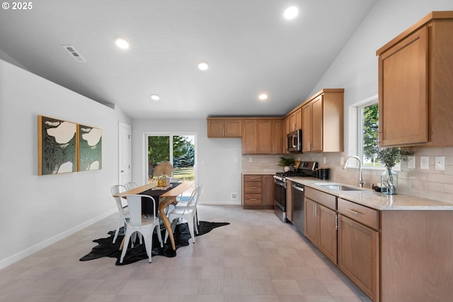 kitchen featuring sink, lofted ceiling, light stone countertops, and stainless steel appliances