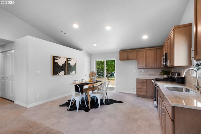 kitchen featuring light stone countertops, appliances with stainless steel finishes, decorative backsplash, sink, and vaulted ceiling