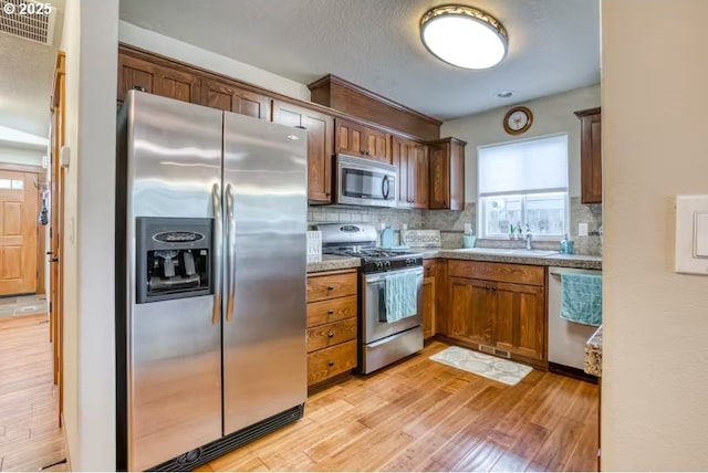 kitchen featuring sink, light hardwood / wood-style flooring, appliances with stainless steel finishes, backsplash, and light stone counters