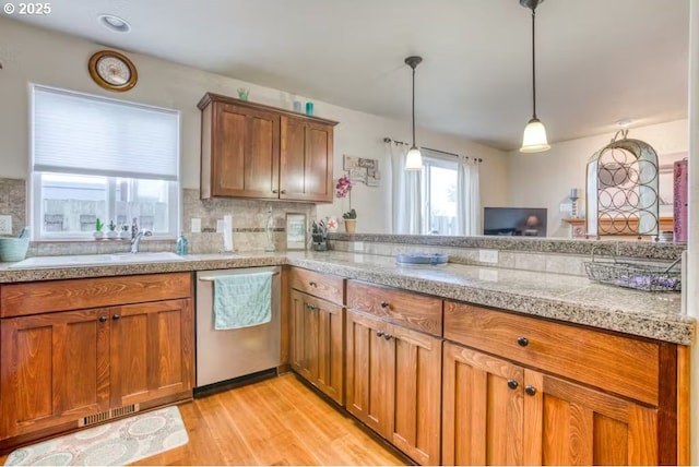 kitchen featuring pendant lighting, sink, tasteful backsplash, stainless steel dishwasher, and light wood-type flooring