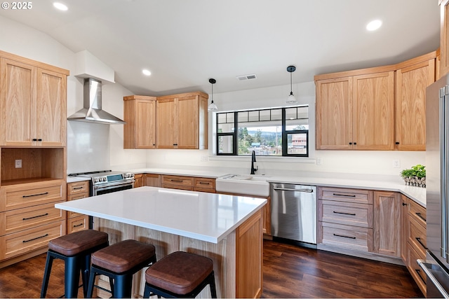 kitchen with appliances with stainless steel finishes, wall chimney range hood, decorative light fixtures, a kitchen island, and sink