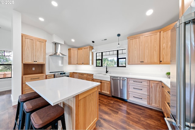 kitchen with wall chimney exhaust hood, hanging light fixtures, appliances with stainless steel finishes, and light brown cabinets