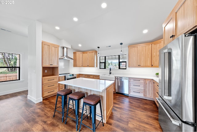 kitchen featuring hanging light fixtures, wall chimney range hood, a kitchen island, stainless steel appliances, and a breakfast bar area