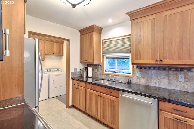 kitchen featuring washing machine and clothes dryer, sink, stainless steel appliances, backsplash, and dark stone counters