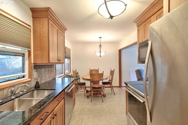 kitchen featuring sink, dark stone countertops, pendant lighting, decorative backsplash, and appliances with stainless steel finishes