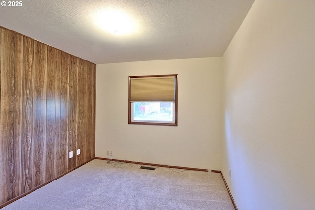 unfurnished room with a textured ceiling, light carpet, and wooden walls