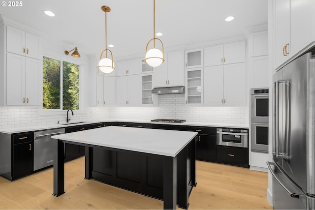 kitchen featuring white cabinets, stainless steel appliances, dark cabinetry, under cabinet range hood, and a sink