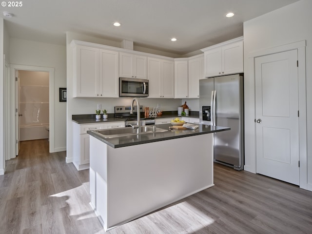 521 Kakela Rd, Winlock, WA 98596 - kitchen with stainless steel appliances, dark countertops, white cabinetry, light wood-style flooring, and an island with sink
