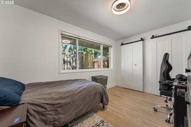 bedroom featuring baseboards, a barn door, and light wood-type flooring