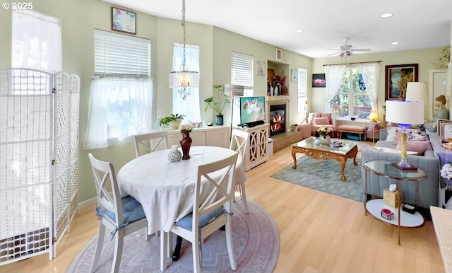 dining area with light wood finished floors, ceiling fan, a glass covered fireplace, a chandelier, and recessed lighting