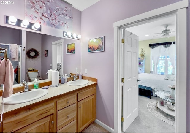 ensuite bathroom with a ceiling fan, double vanity, baseboards, and toilet