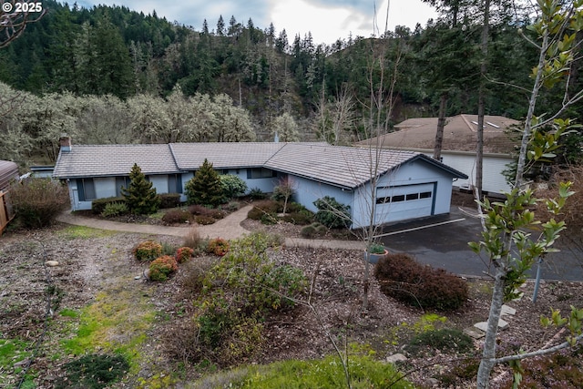 ranch-style home with a garage, driveway, and a wooded view