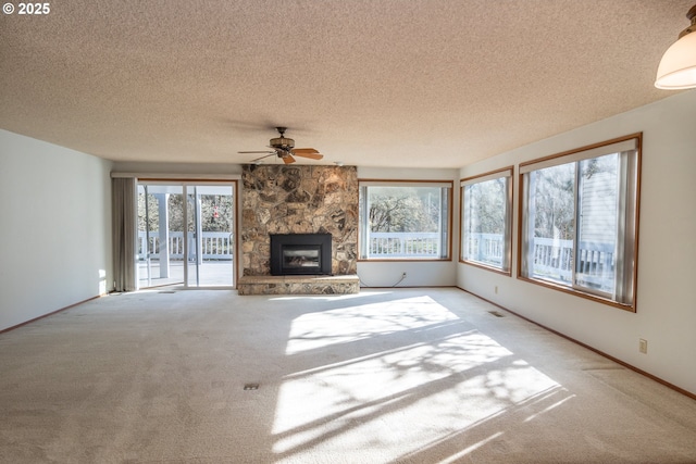 unfurnished living room featuring a textured ceiling, a stone fireplace, carpet flooring, a ceiling fan, and baseboards