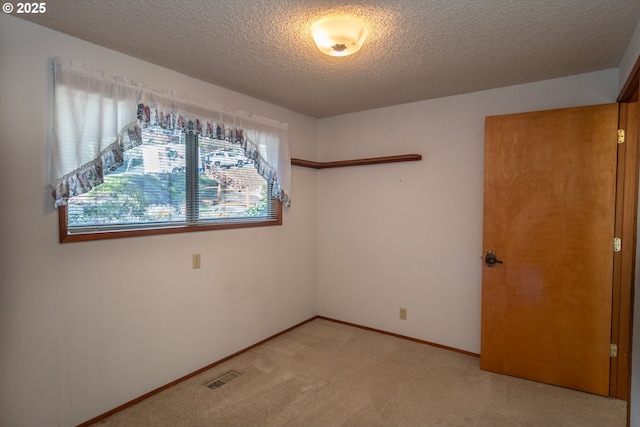 spare room with light carpet, baseboards, visible vents, and a textured ceiling