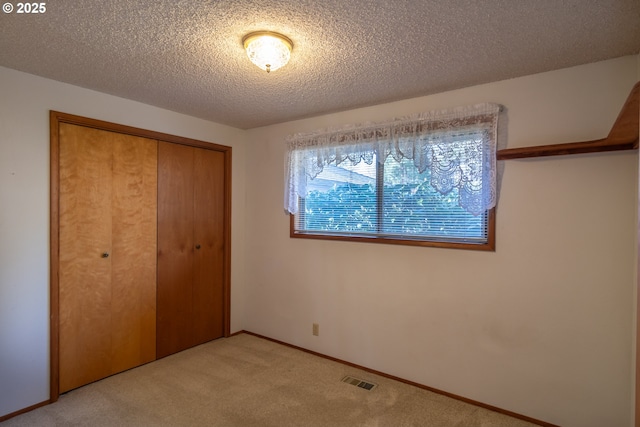 unfurnished bedroom featuring a textured ceiling, light carpet, visible vents, baseboards, and a closet
