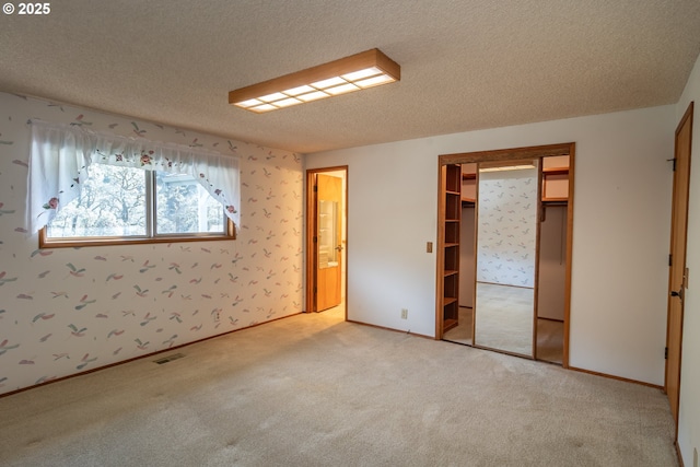 unfurnished room with visible vents, light carpet, a textured ceiling, and wallpapered walls
