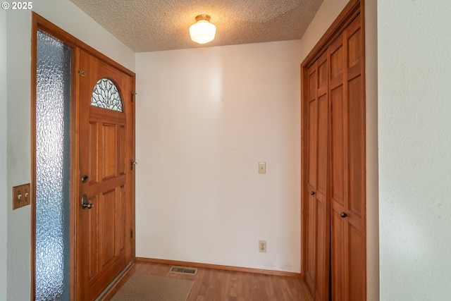 entrance foyer with baseboards, a textured ceiling, visible vents, and wood finished floors