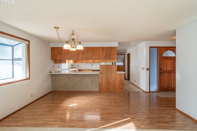 kitchen featuring tasteful backsplash, brown cabinets, a peninsula, an inviting chandelier, and a sink