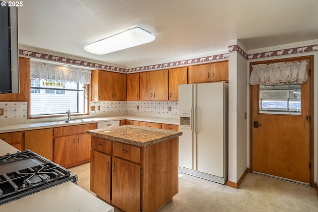 kitchen featuring white appliances, a kitchen island, a sink, backsplash, and brown cabinets