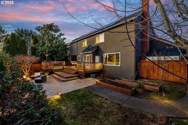 back house at dusk featuring a wooden deck, an outdoor hangout area, and a patio