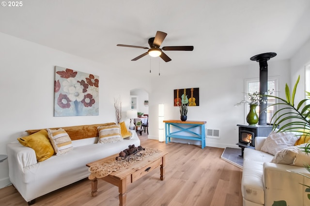 living room featuring light hardwood / wood-style flooring, ceiling fan, and a wood stove