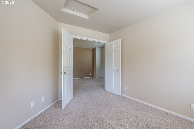unfurnished room with light colored carpet, attic access, and baseboards