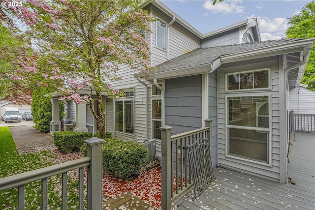 entrance to property featuring central AC, a wooden deck, and a shingled roof