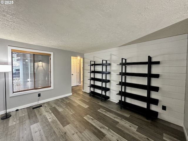 spare room featuring baseboards, visible vents, dark wood finished floors, and a textured ceiling