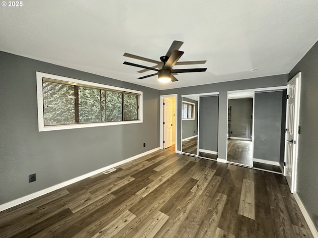 unfurnished bedroom with visible vents, baseboards, ceiling fan, dark wood-type flooring, and multiple closets