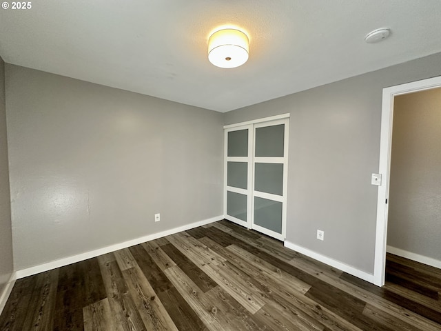 spare room featuring baseboards and dark wood-type flooring