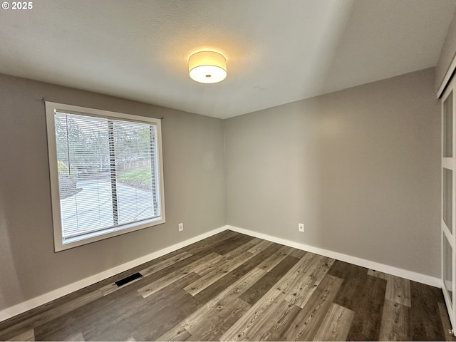 spare room featuring dark wood-type flooring, visible vents, and baseboards