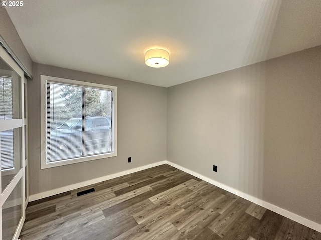 empty room with dark wood-type flooring, visible vents, and baseboards