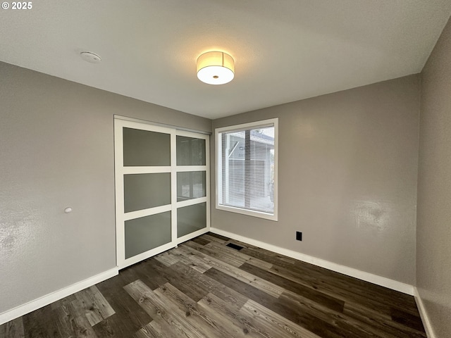 empty room with dark wood-type flooring, visible vents, and baseboards