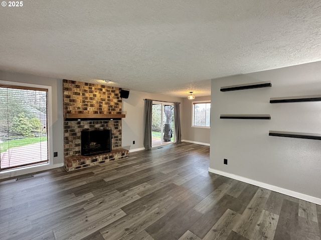 unfurnished living room featuring a textured ceiling, visible vents, baseboards, a brick fireplace, and dark wood-style floors