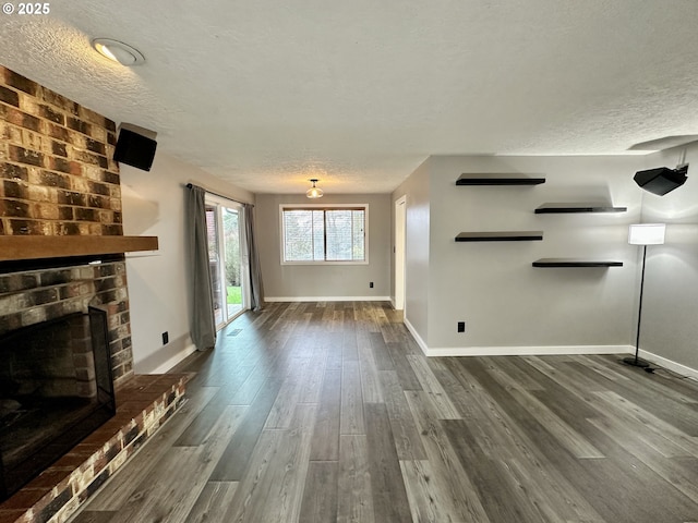 unfurnished living room featuring a brick fireplace, a textured ceiling, baseboards, and wood finished floors